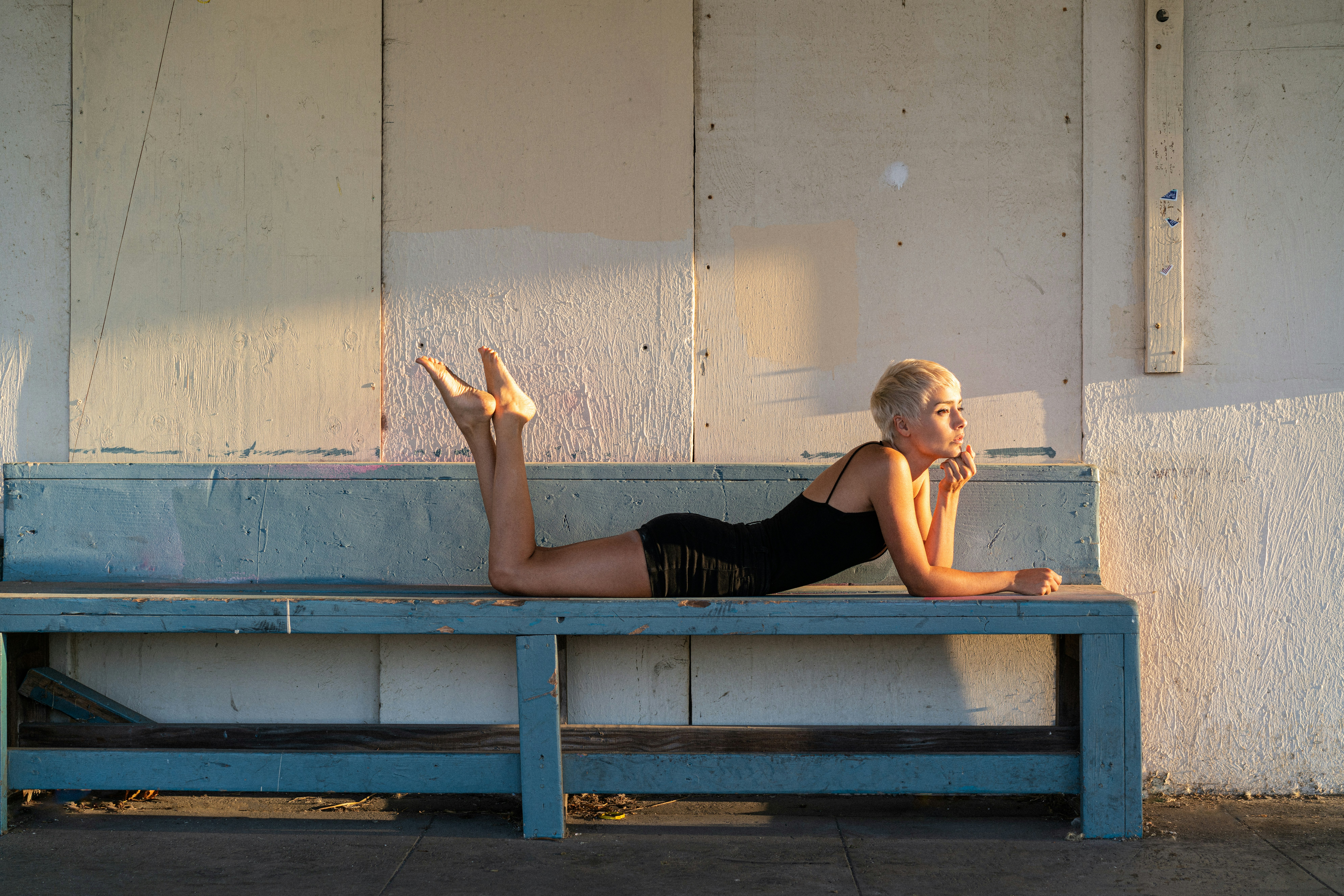woman in black tank top and black shorts lying on blue wooden bench